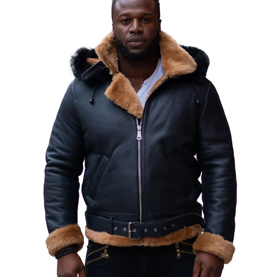 Front view of a man wearing Jean's B3 Bomber Aviator Shearling Jacket with hoodie, featuring sleek black leather with contrasting tan shearling lining around the collar and cuffs. The jacket includes a front zipper closure and leather belt detailing at the waist, perfect for colder weather.