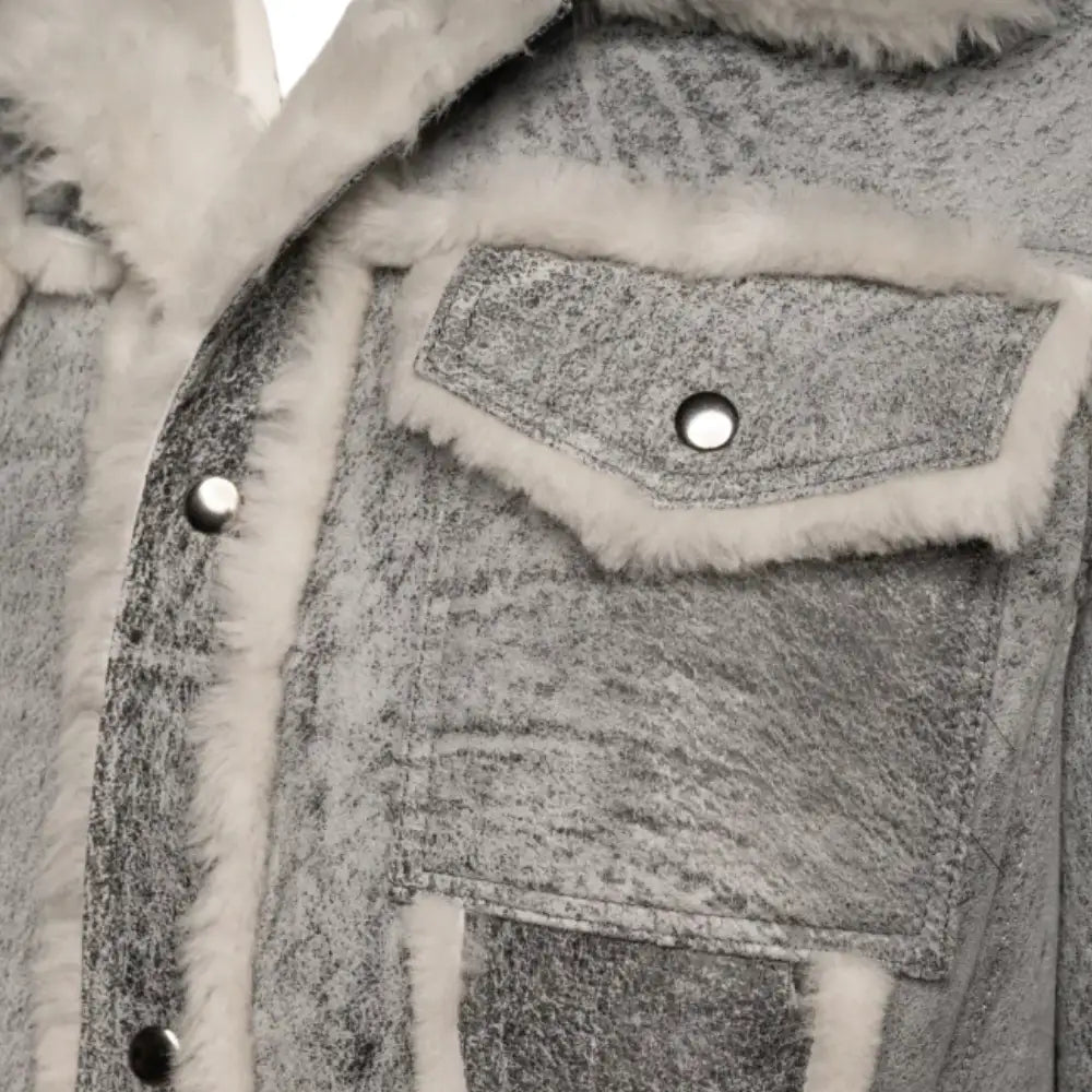 Close-up of Aiden's Grey Trucker Jacket showcasing the chest pocket with a snap button closure. The grey distressed fabric is complemented by the white shearling trim along the pocket and collar, adding a vintage touch.
