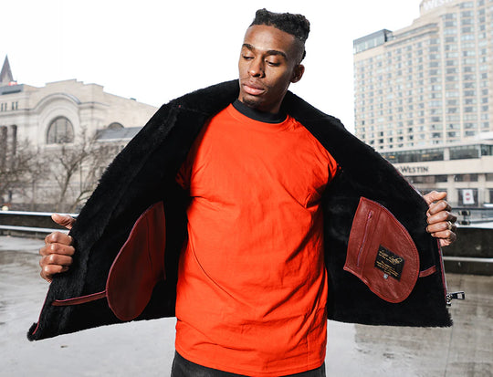 A man showcasing interior of Burgundy B3 Bomber Shearling Jacket over an orange shirt in an urban winter setting.