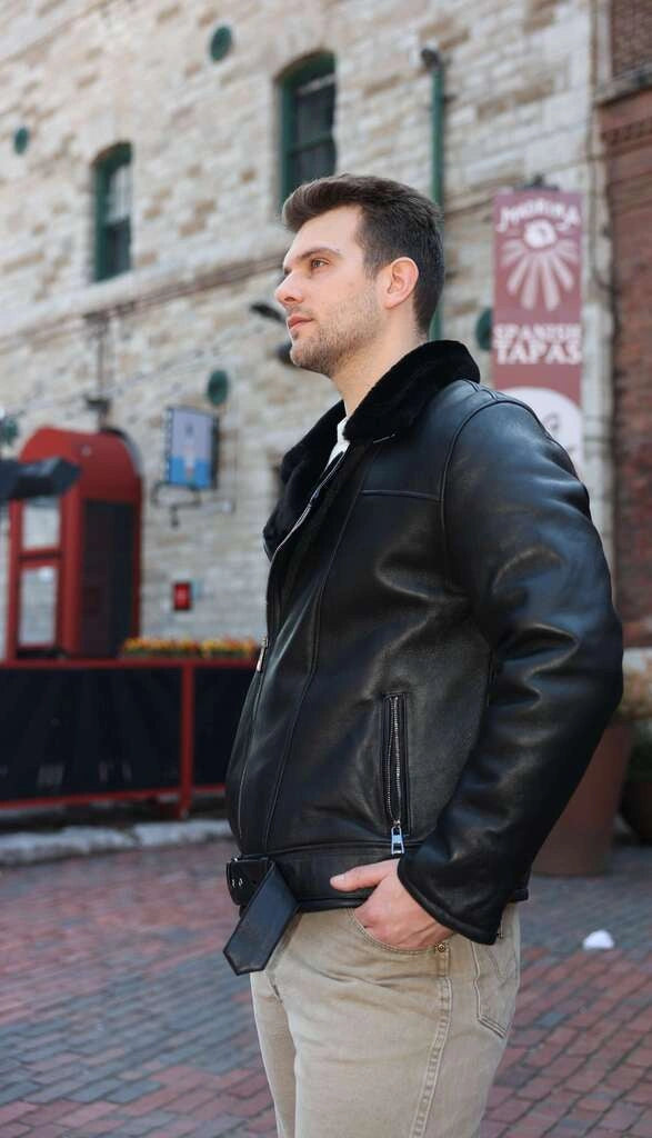 Man wearing Black on Black Belted Shearling Leather Biker Jacket standing on a street with a brick building in the background