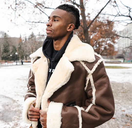 Man wearing a brown shearling overcoat with white fur lining in a snowy outdoor setting