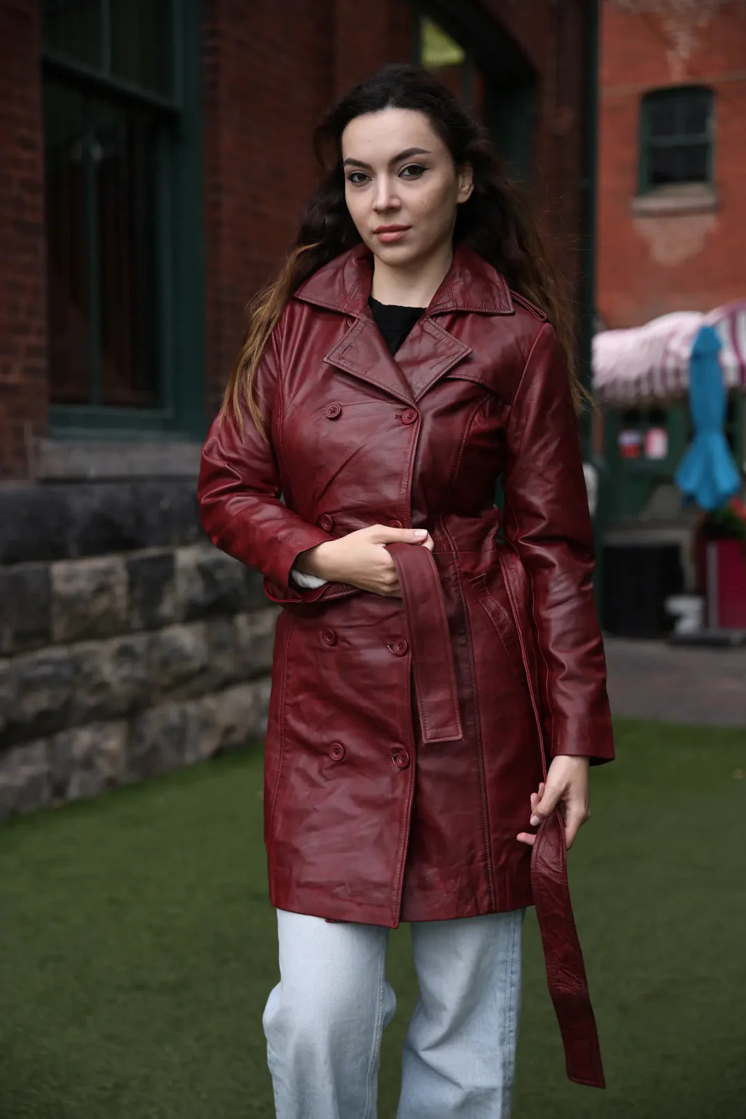 Side profile shot of a model in the coral red leather coat, highlighting the flattering cinched waist and the mid-length drape.