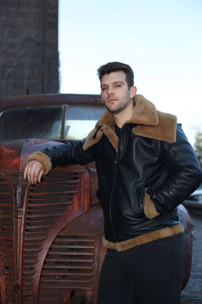 Man wearing a Graysen black Aviator bomber shearling jacket with brown fur trim leaning against an old car.