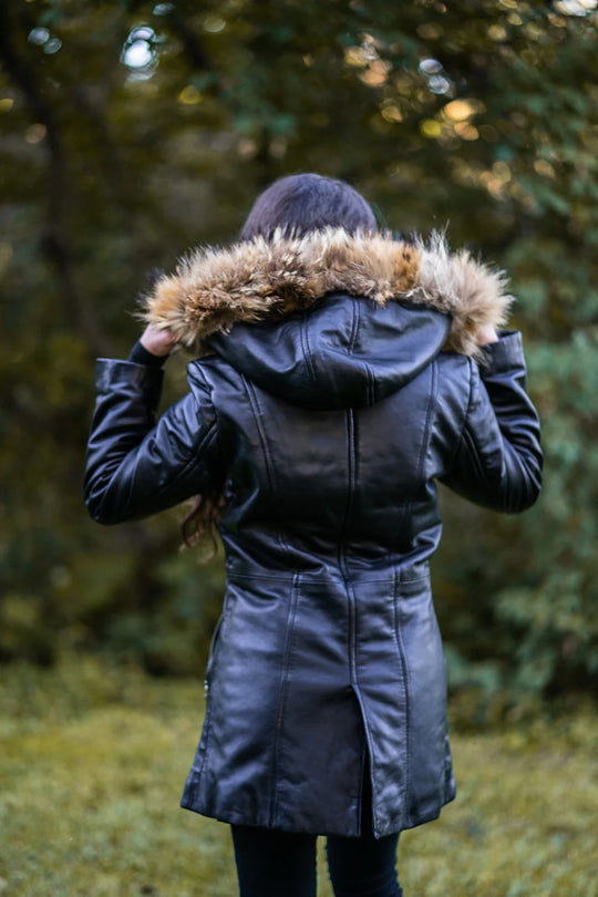 Woman back profile in Jazmyn's long winter coat, emphasizing the thick fox fur hood and the protective longline fit in a forest setting.