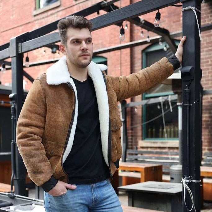 Man wearing a Lucian's distressed brown A2 Bomber shearling jacket and blue jeans standing on a rooftop patio.