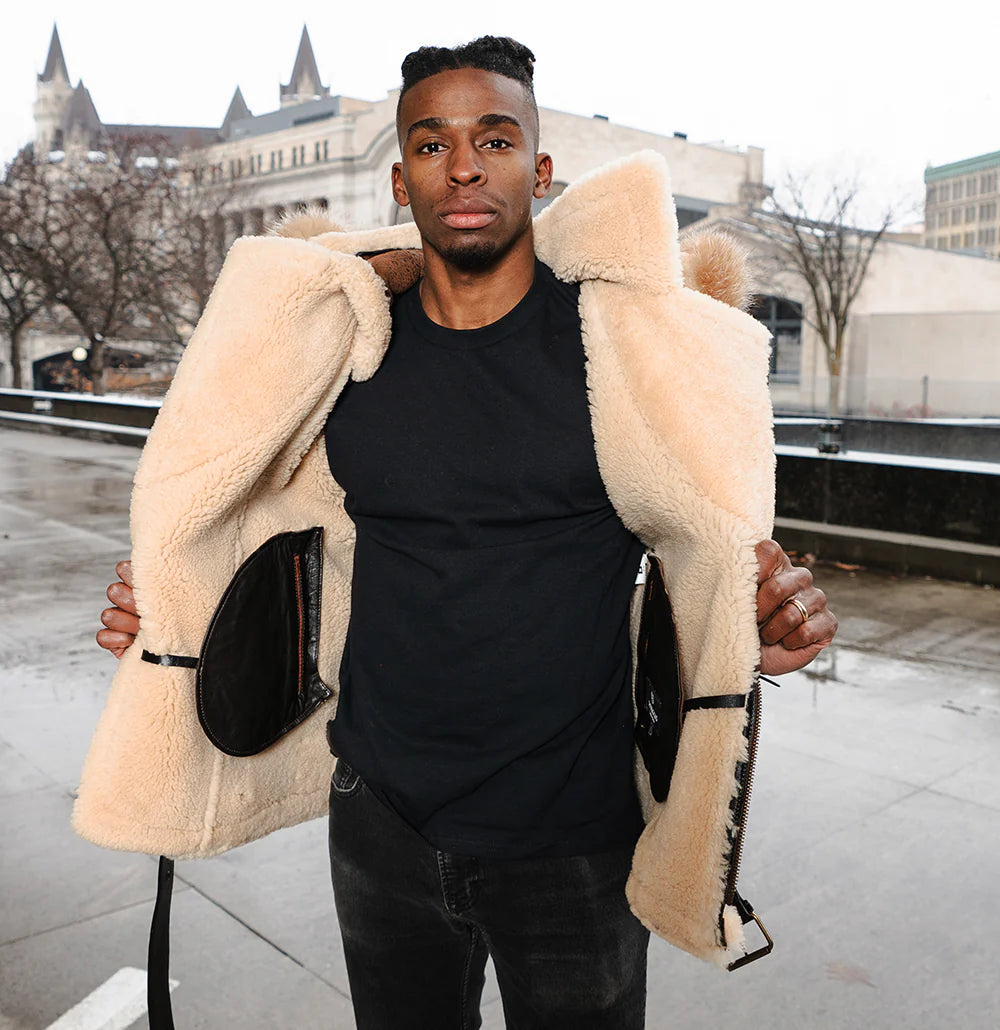 Lifestyle image of a model wearing Ridgeway's Vintage Distressed Brown Shearling Vest with a cozy shearling-lined hoodie. The rugged brown leather vest features soft beige faux fur lining, with the model standing outdoors in a stylish urban setting.