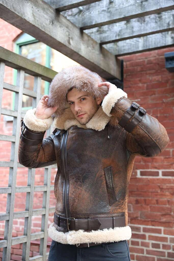 Man wearing Rocco vintage brown aviator shearling jacket with fur trim hoodie against a brick wall.