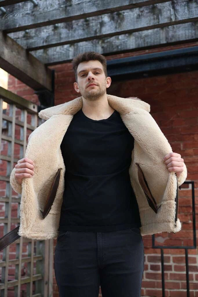 Man wearing Rocco vintage brown aviator shearling jacket showcasing interior of the shearling in front of a brick wall.