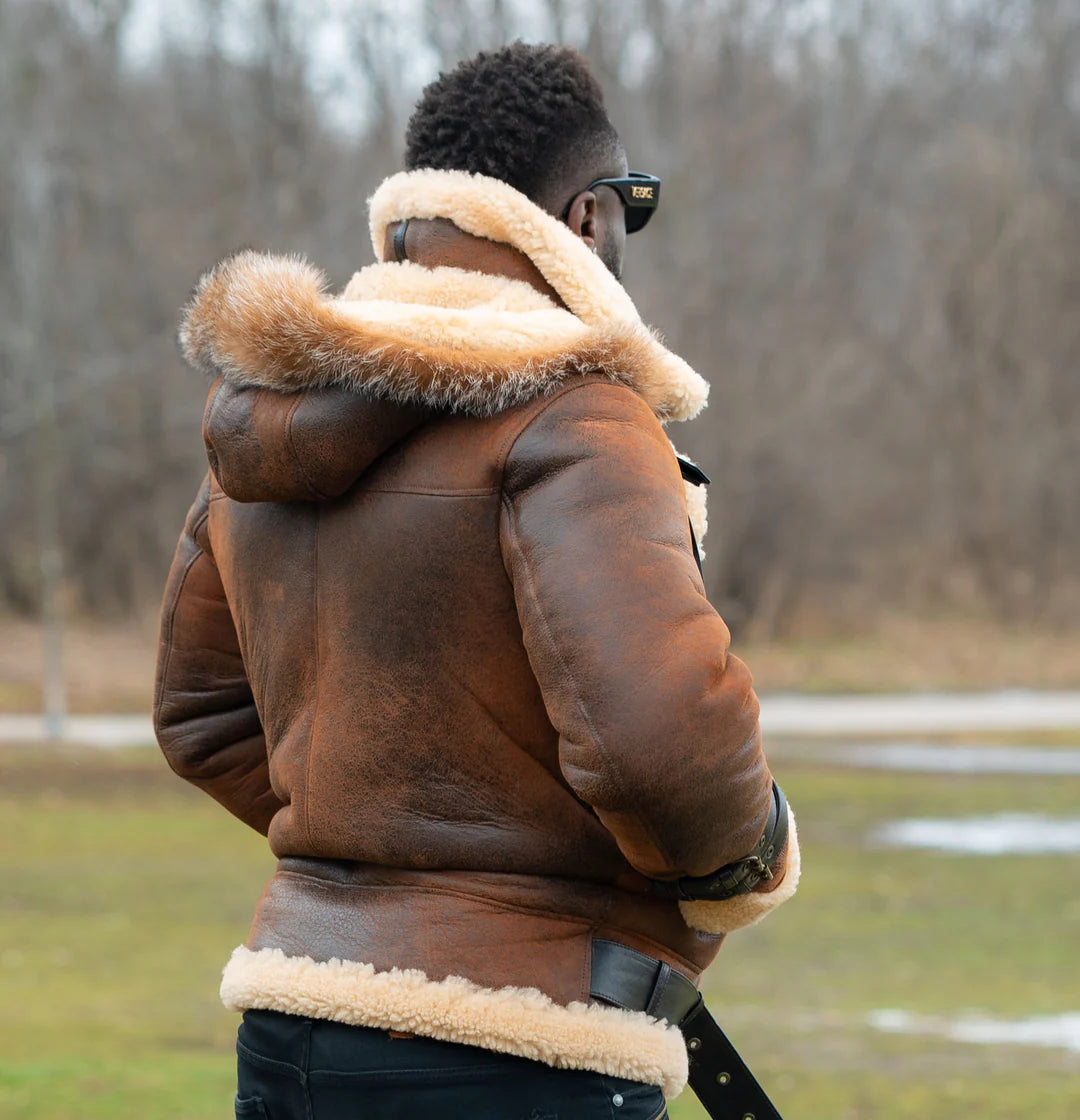 Lifestyle photoshoot of a man wearing showcasing back view of Rocco vintage brown aviator shearling jacket featuring a classic cream shearling collar and fur hoodie in an outdoor setting.